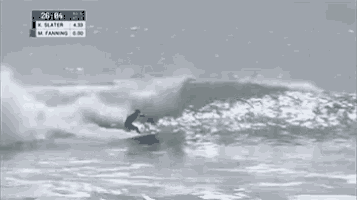 a surfer is riding a wave in the ocean with a scoreboard behind him that says k slater
