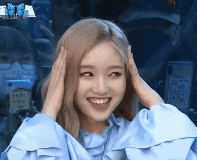 a woman in a blue shirt is smiling and holding her hands to her head