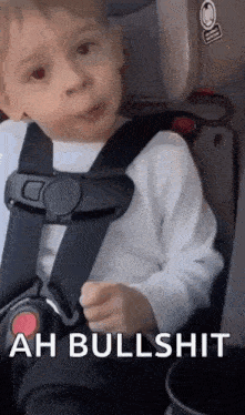 a little boy is sitting in a car seat and making a face .
