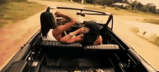 a woman is laying on top of a man in a convertible car .
