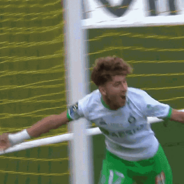 a man in a white shirt and green shorts celebrates a goal