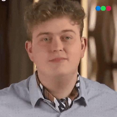 a young man with curly hair is wearing a blue shirt and a scarf around his neck