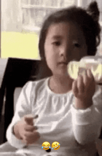 a little girl is sitting at a table with a spoon in her hand and making a funny face .