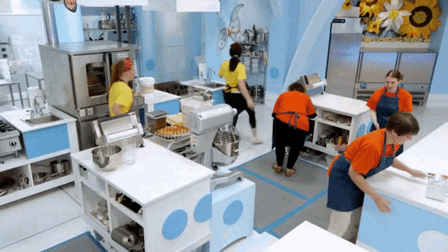 a group of women are working in a kitchen with a sunflower on the wall