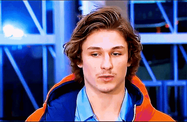 a young man with long hair and a blue shirt is wearing an orange jacket