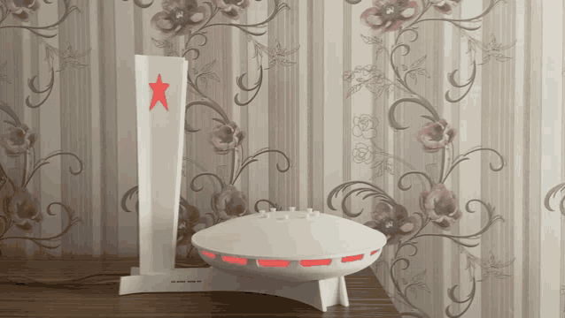 a white object with a red star on top of it is on a table in front of a floral wallpaper