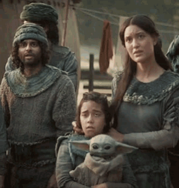 a woman is holding a baby yoda in her arms while a group of people are standing behind her .