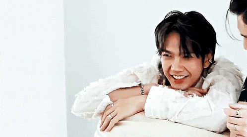 a man wearing a white fur coat is smiling while sitting on a couch .