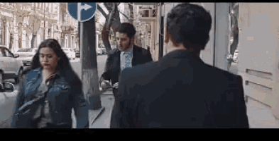 a man in a suit and a woman in a denim jacket are walking down a sidewalk .