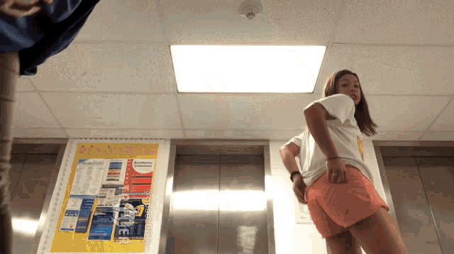 a woman stands in front of an elevator with a poster on the wall that says ' admissions ' on it