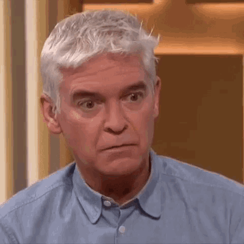 a man with gray hair is wearing a blue shirt and making a face .