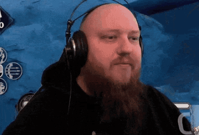 a bald man with a beard wearing headphones and a black shirt with the letter c on it