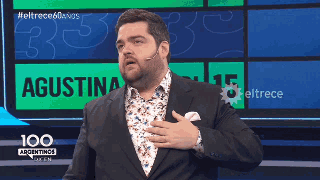 a man in a suit stands in front of a screen that says 100 argentinas dicen