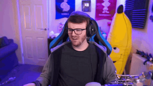 a man wearing glasses and headphones is sitting in a chair in front of a yellow stuffed banana .