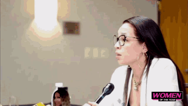 a woman speaking into a microphone with the words women of the year on the bottom right