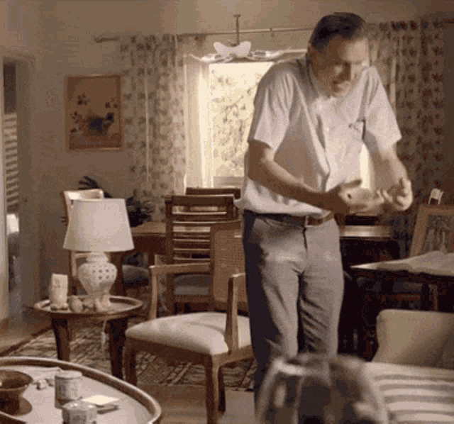 a man in a white shirt is standing in a living room holding something