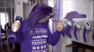 a woman with purple hair is wearing a purple sweater that says gladiator on it .