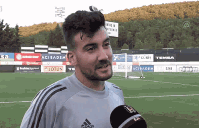 a man wearing an adidas shirt talks into a microphone
