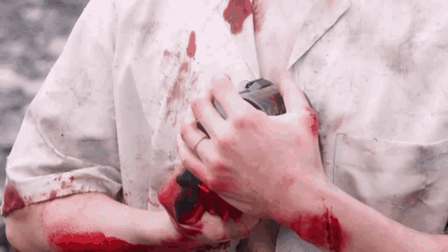 a person with blood on their shirt is holding a camera in their hands .