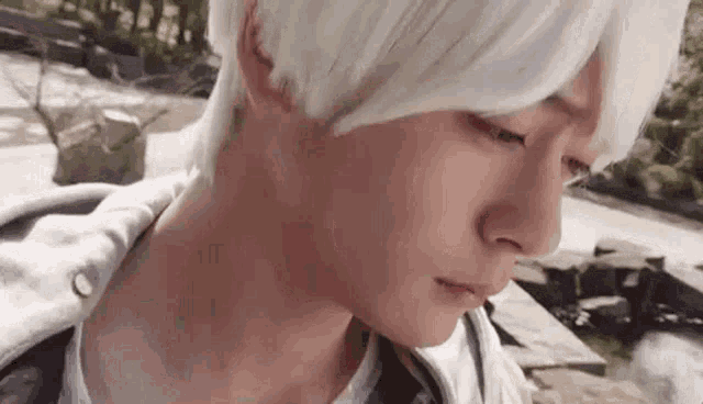 a close up of a person 's face with white hair and a gray jacket .