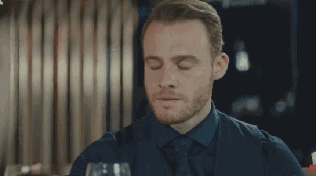 a man with his eyes closed is sitting at a table with a glass of wine