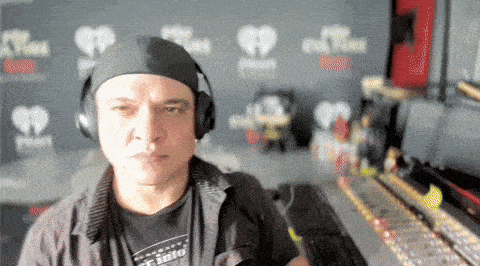 a man wearing headphones and a bandana is sitting in front of a wall that says iheartradio