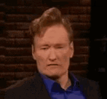 a man in a suit and blue shirt is making a funny face and sticking his tongue out .