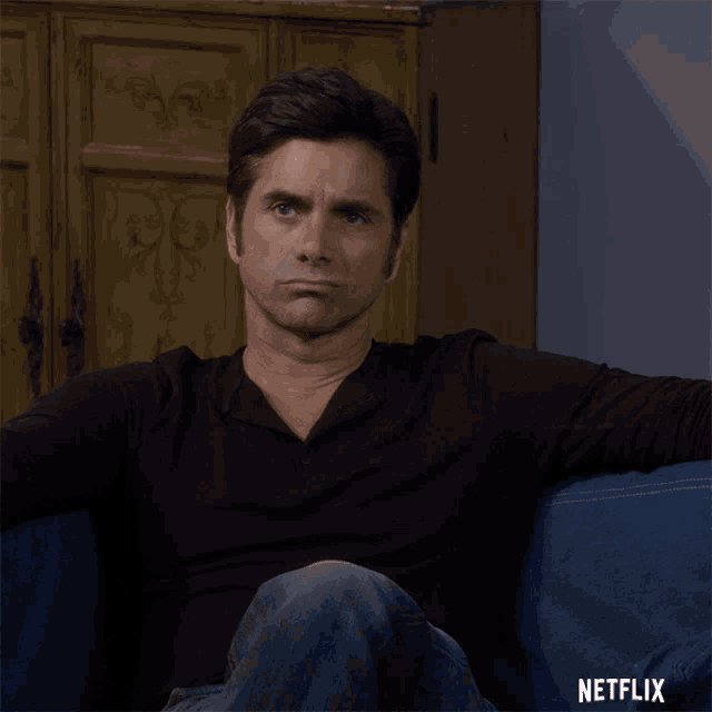 a man is sitting on a blue couch with a netflix logo behind him