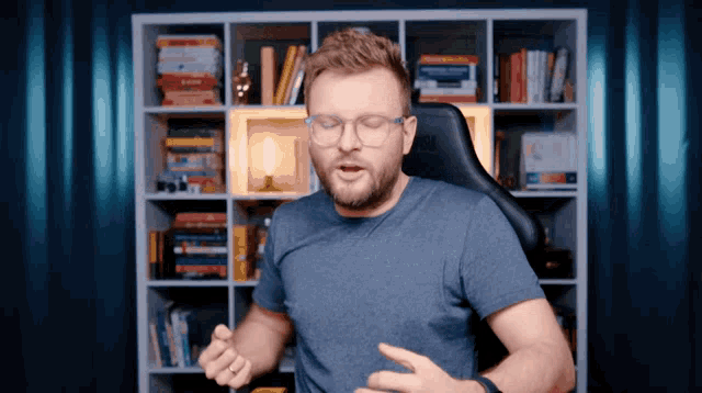 a man wearing glasses and a blue shirt is sitting in front of a bookcase