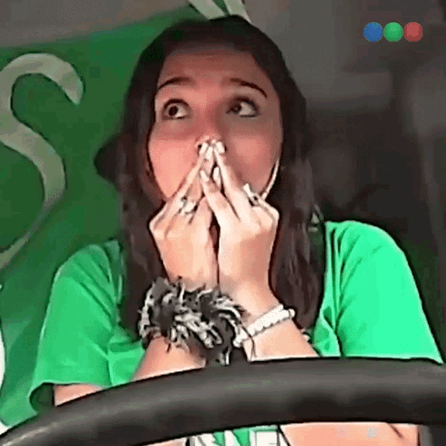 a woman wearing a green shirt is covering her mouth with her hands
