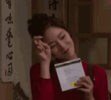 a woman in a red shirt is holding a piece of paper in her hand .