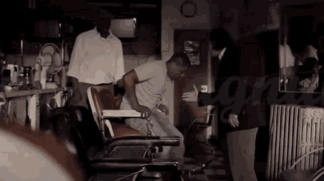 a man is getting his hair cut in a barber shop while a man in a suit looks on