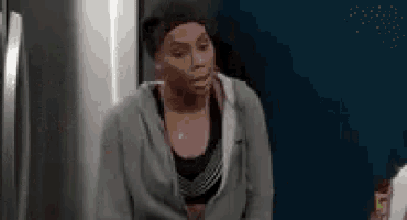 a woman is standing in front of a refrigerator in a kitchen wearing a hoodie and a headband .