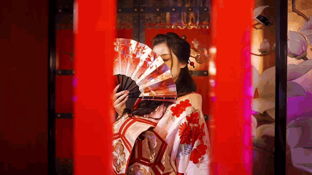 a woman in a white and red kimono holds a fan in front of her face