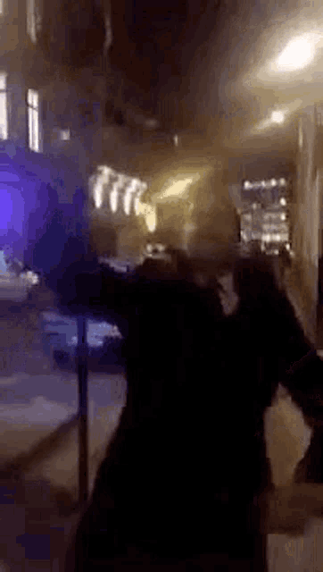 a man is walking down a street at night with his arms outstretched in front of a building .
