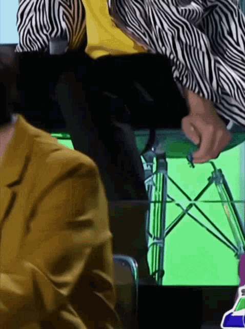 a man in a zebra print shirt is sitting at a table with a green screen in the background .