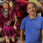 a man in a blue shirt is standing in front of a group of people in carnival costumes .