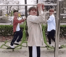 a man is hanging from a bar in a park with other people