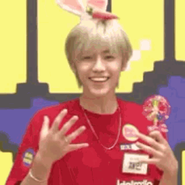 a young man wearing a red shirt and a bunny ear hat is smiling and holding a trophy .