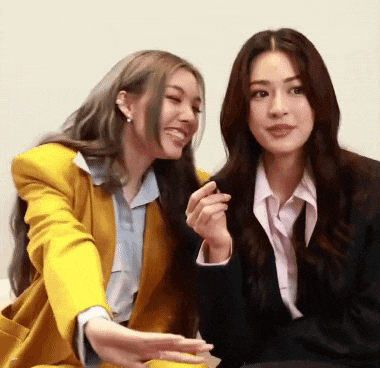two women are sitting next to each other and laughing . one of the women is wearing a yellow jacket .