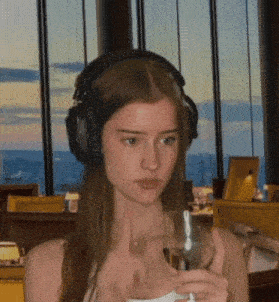 a girl wearing headphones holds a glass of wine