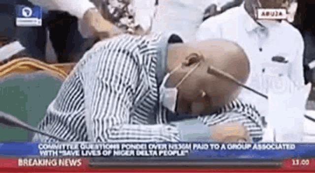 a man wearing a mask is sleeping in front of a microphone on a news channel .