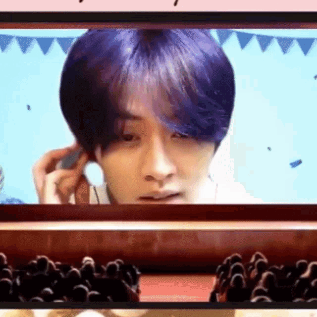 a man with purple hair is sitting in front of a crowd of people on a stage .