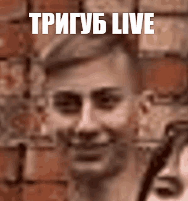 a man is smiling in front of a brick wall with the word live written above him