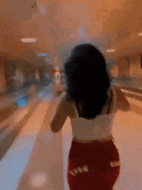 a woman is walking down a bowling alley wearing red shorts and a white tank top .