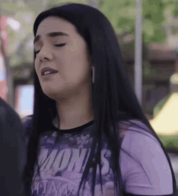 a woman with long black hair is wearing a purple shirt that says mon 's
