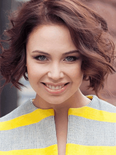 a woman wearing a yellow and gray striped shirt smiles for the camera