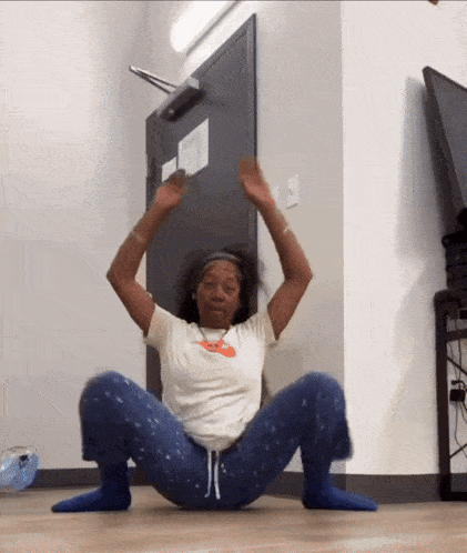 a woman in a nike shirt is squatting on the floor with her arms in the air