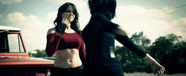 a woman in a red crop top stands next to another woman in a black top