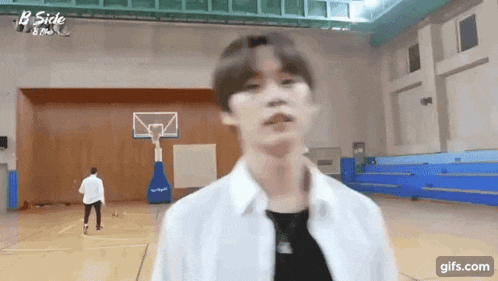 a man in a white shirt is standing in a basketball court with a basketball hoop in the background .